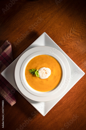 Organic homemade soup in white bowl, in earthy setting on wooden dining table