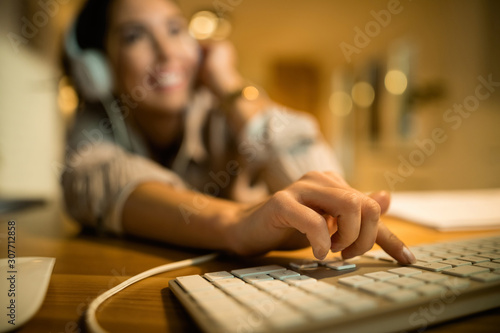 Close-up of woman typing on computer keyboard in the evening at home.