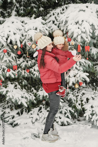 Fototapeta Naklejka Na Ścianę i Meble -  Christmas family in winter park. Happy family mother and child daughter having fun, playing at winter walk outdoors. Outdoor family fun on Christmas vacation.Winter clothing for baby and toddler.