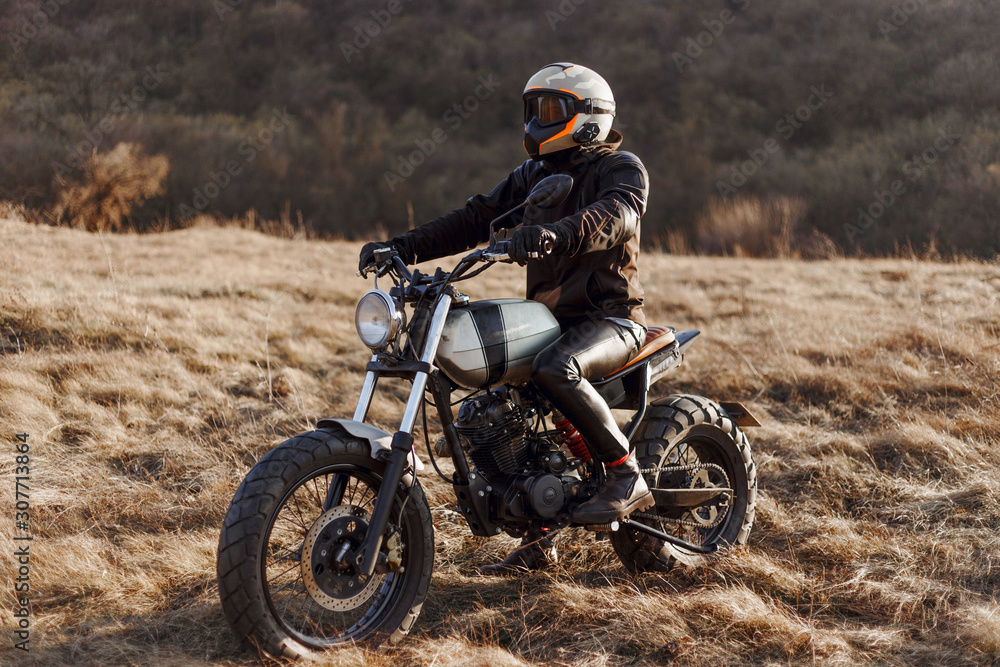 The single man-equipped, motorcyclist drives in the steppe, wearing a helmet, black jacket, gloves, leather pants and boots. Hobby, extreme occupation, recreation in nature, freedom.