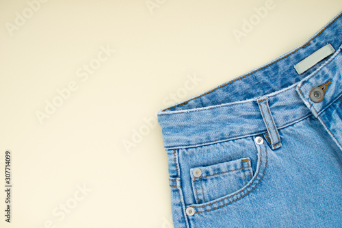 Light blue mom denim jeans with pocket at ivory color pastel background. Modern fashion flat lay.