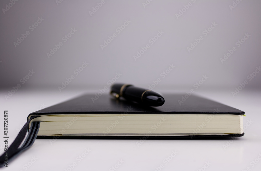 Low angle close up of a black pen on top of a closed black notebook Low angle close up of a black pen on top of a closed black notebook