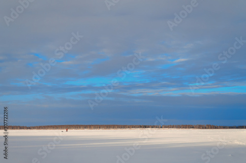 A lonely small man walks under a turquoise sky through a snowy field. The horizon between the sky and the snow field divides the frame in a ratio of one to four. You can place text on top.