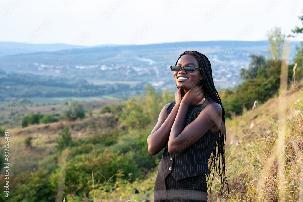 Naklejka premium Close up portrait of the young happy african girl in black clothes and sunglasses that smiling and looking at the camera