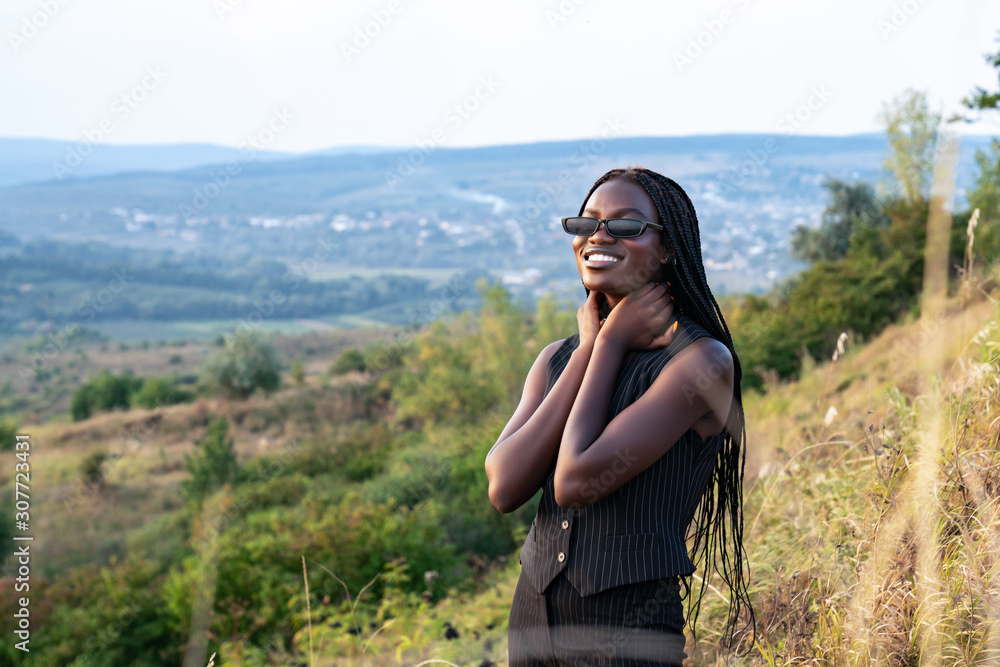 Close up portrait of the young happy african girl in black clothes and sunglasses that smiling and looking at the camera
