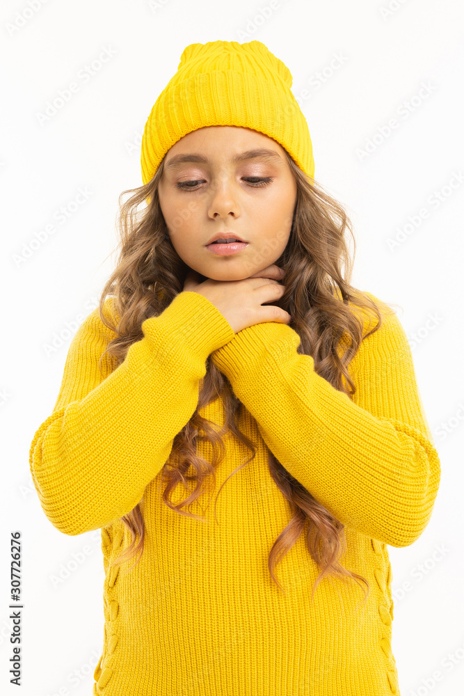 European attractive girl in a yellow hat and jacket holds hands near the throat on a white studio background European attractive girl in a yellow hat and jacket holds hands near the throat on a white studio background