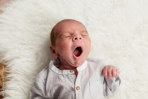 bebe de 3 semanas (menos de un mes) bostezando, bostezo de niño pequeño tumbado en alfombra de pelos blancos y vestido de lino. photo