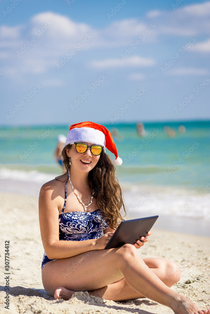 girl in santa claus hat on the beach with laptop, tablet girl in santa claus hat on the beach with laptop, tablet