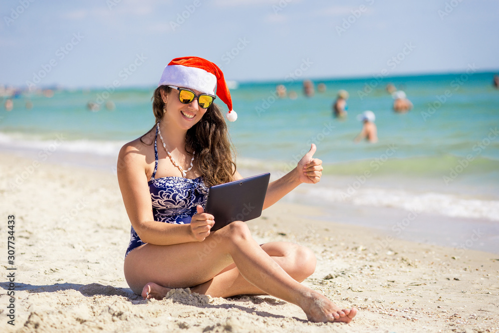 girl in santa claus hat on the beach with laptop, tablet girl in santa claus hat on the beach with laptop, tablet