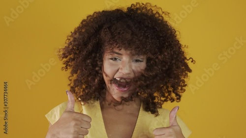 Happy laughing American African woman with her cyrly hair in yellow background. Laughing curly woman in sweater touching her hair and looking at the camera. photo