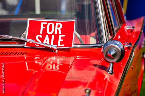 FOR SALE, red sign on classic antique American bright red car windscreen and chrome parts close up, during outdoor old cars show