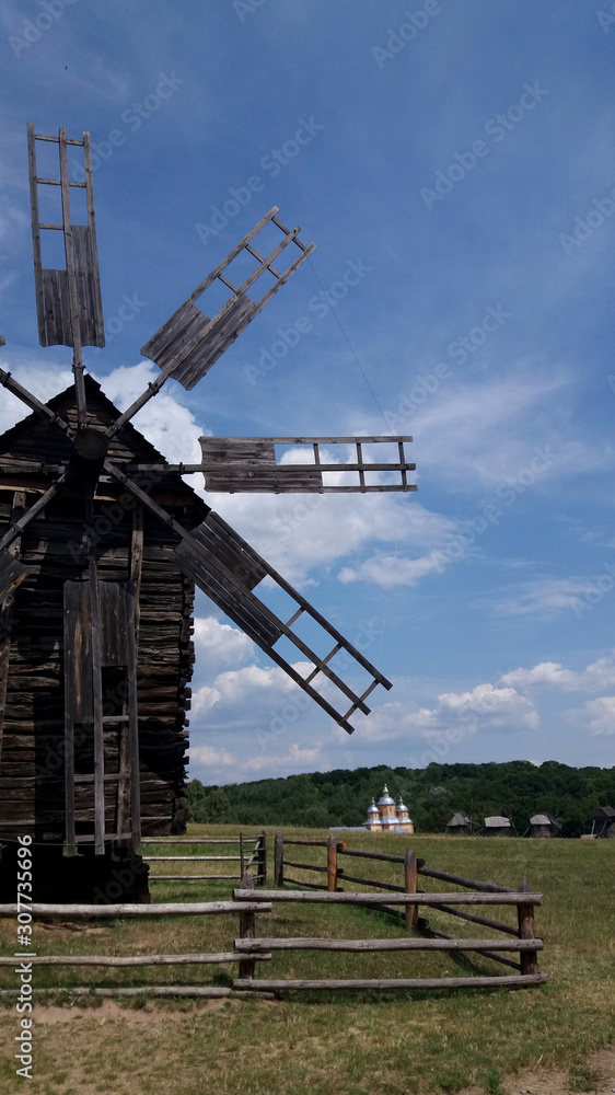 Old mill on a background of blue sky and landscape. A photography of a historic cereal milling device.