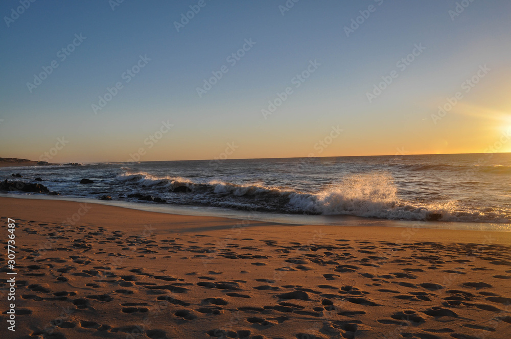 Orange sunset over the ocean. Waves in sunlight. Sandy beach which reflects the sunset. Winter sunset on beach