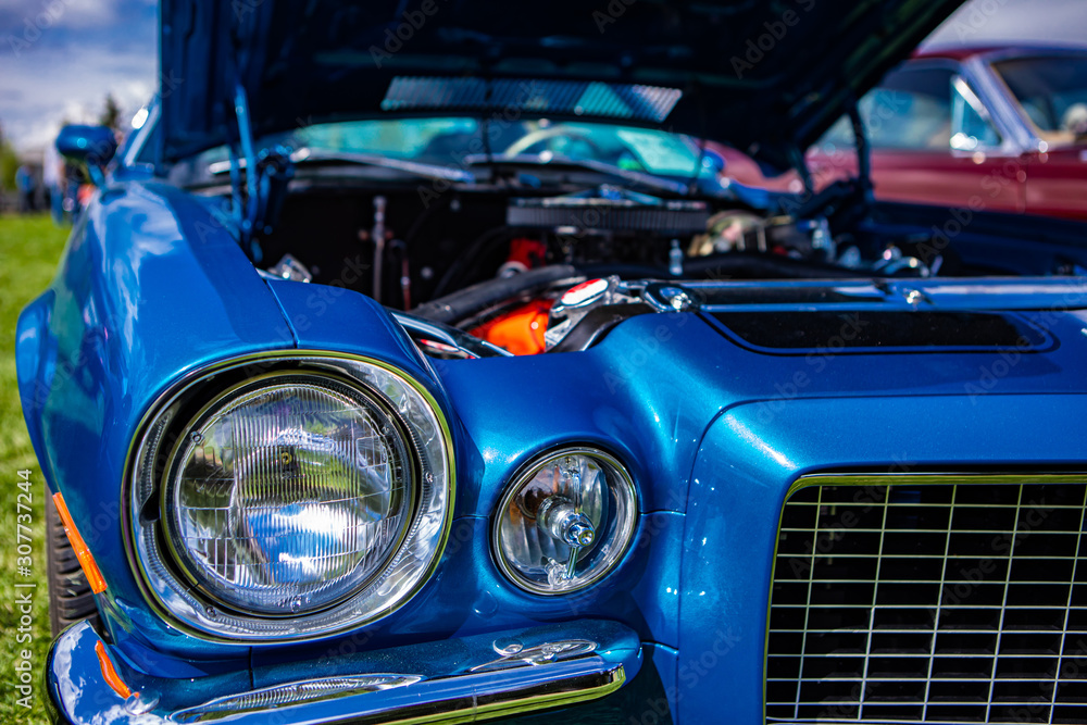 selective focus on an old vintage American muscle blue car half front, left side, with open hood, headlights light lamps close up