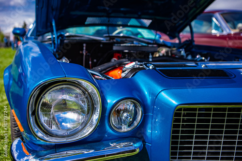 selective focus on an old vintage American muscle blue car half front, left side, with open hood, headlights light lamps close up