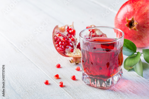 Glass of pomegranate juice and ripe pomegranate on a white wooden background. Healthy drink concept. Сopy space