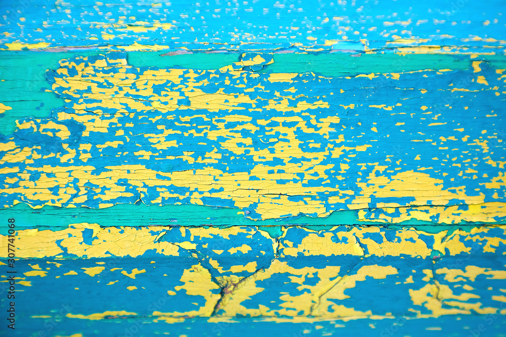 Yellow-blue-green peeling paint texture. A wooden surface covered with several layers of cracked paint