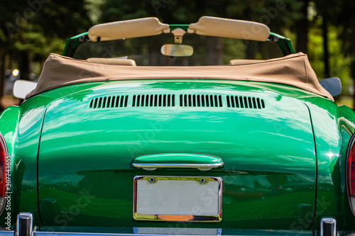 classic antique American green Convertible car rear selective focus with open roof against blurred trees background, during outdoor old cars show