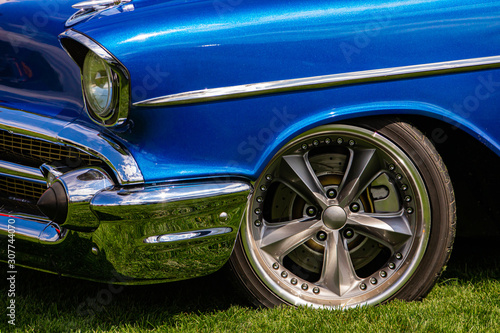 Old antique classic American blue car front on the grass with a chrome bumper and body parts, front wheel side close up view, sports star wheel rim