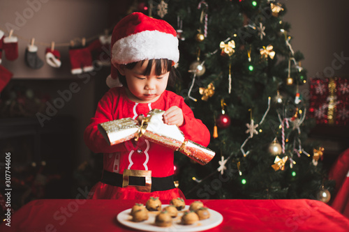 toddler girl playing Christmas cracker in front of christmas tree at home © M-image