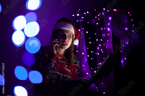 girl student in Christmas clothes sitting at night with a laptop and talking on the phone, she communicates online at Christmas