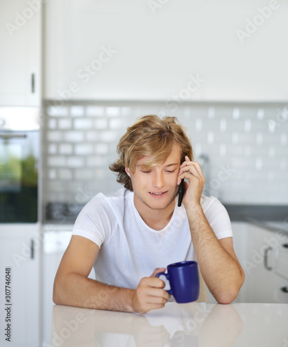 Teenage boy typing text message.Sitting in the kitchen.Using smart phone