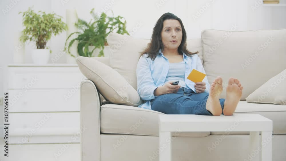 Attractive woman is watching the TV with anticipation. She compares the information on paper sticker and on TV. Copy space. 4K. Attractive woman is watching the TV with anticipation. She compares the information on paper sticker and on TV. Copy space. 4K.
