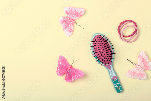 Little girl's hair rubber bands, comb and decorative butterflies on bright yellow background. Flat lay, top view, text space.