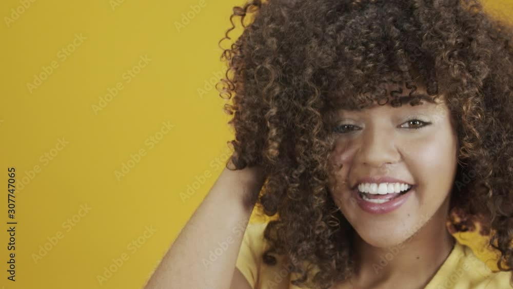 Happy laughing American African woman with her cyrly hair in yellow background. Laughing curly woman in sweater touching her hair and looking at the camera. Happy laughing American African woman with her cyrly hair in yellow background. Laughing curly woman in sweater touching her hair and looking at the camera.