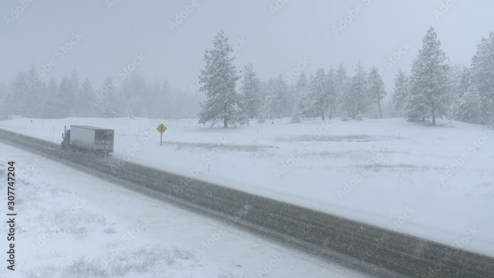 Semi-truck drives a heavy cargo container across the state of Washington through a raging snowstorm. Commercial lorry transporting goods through the horrible weather condition on a freezing winter day Semi-truck drives a heavy cargo container across the state of Washington through a raging snowstorm. Commercial lorry transporting goods through the horrible weather condition on a freezing winter day