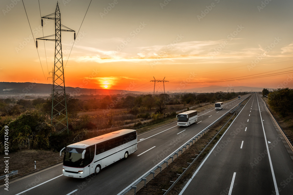 Caravan or convoy of Four buses in line traveling on a country highway under amazing orange sunset sky. Highway transportation with white buses Caravan or convoy of Four buses in line traveling on a country highway under amazing orange sunset sky. Highway transportation with white buses
