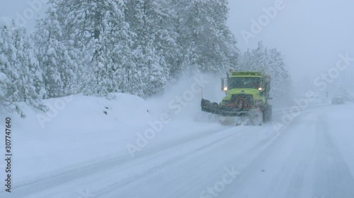 CLOSE UP: Truck plows the snowy country road during a horrible snowstorm raging in the state of Washington. Cars carefully drive behind a snow plough clearing the road during a devastating blizzard.