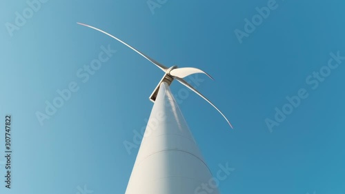 Slow motion of the blades of a large wind turbine in a field against a blue sky on a sunny summer day. View from the bottom up. Alternative energy sources. Windy park. Ecological energy. Industrial