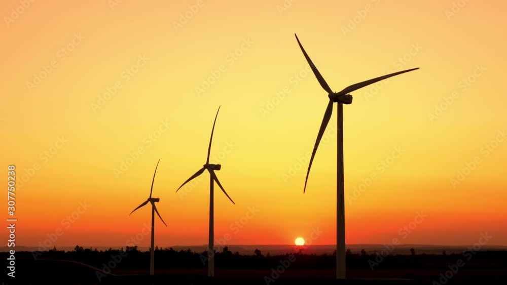Motion the blades of a large wind turbine in a field against a background of orange sunset on the horizon with a bright disk sun. Alternative energy sources. Windy park. Ecological energy.Industrial Motion the blades of a large wind turbine in a field against a background of orange sunset on the horizon with a bright disk sun. Alternative energy sources. Windy park. Ecological energy.Industrial