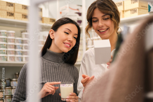 Young smiling consultant happily helping to choose aroma candle to pretty Asian girl in store photo