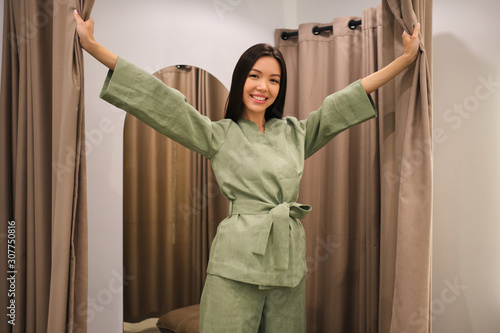 Attractive smiling Asian girl in stylish suit joyfully posing in dressing room of clothes store