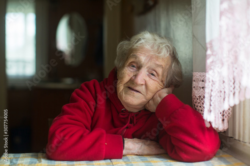 Portrait of old woman sitting at a table in the house.