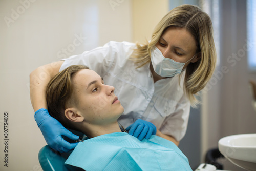 Young man patient sitting in a chair and woman dentist in dental room.