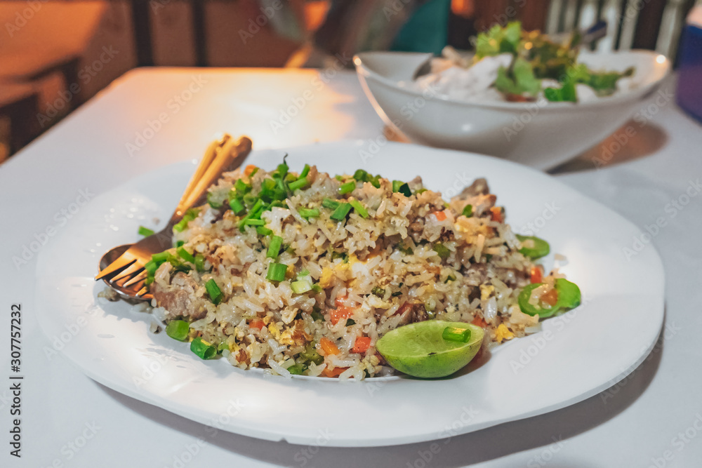Asian fried rice with eggs, chicken, carrots, green onions and other vegetables and decorated with a slice of lime on the blurred cafe background.