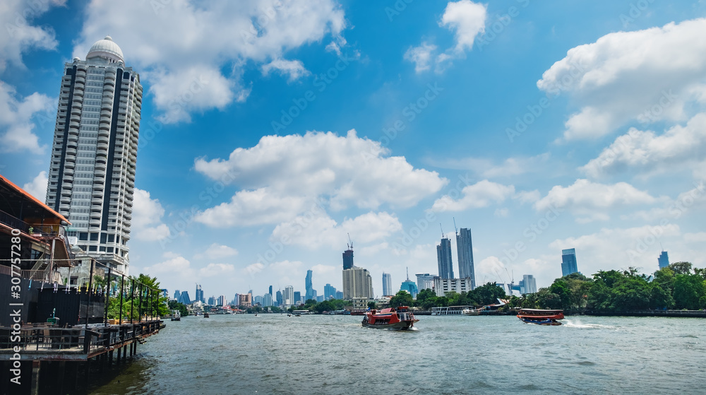 Fototapeta premium Tourist popular boat travel on the Chao Phraya river, Bangkok, Thailand. Bangkok city buildings cityscape. Skyscrapers of western bank of Chao Praya River are seen on the horizon.