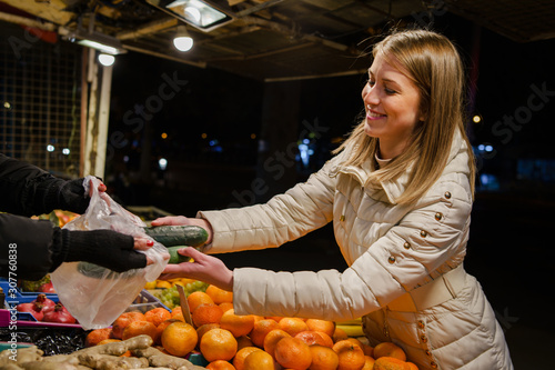 One young caucasian woman female girl picking and buying some fresh vegetables at the local market in the city at in autumn spring or winter night cucumbers