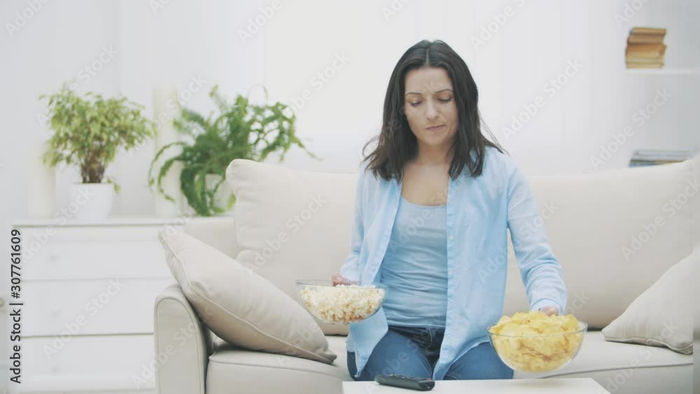 Happy woman is holding huge deep plates with pop corn and chips. Pretty woman is chewing pop corn. 4K. Happy woman is holding huge deep plates with pop corn and chips. Pretty woman is chewing pop corn. 4K.