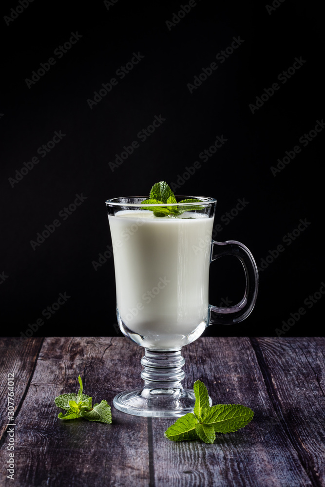 Ayran in a glass, sour-milk drink, yogurt, decorated with a leaf of mint. On a wooden background Ayran in a glass, sour-milk drink, yogurt, decorated with a leaf of mint. On a wooden background