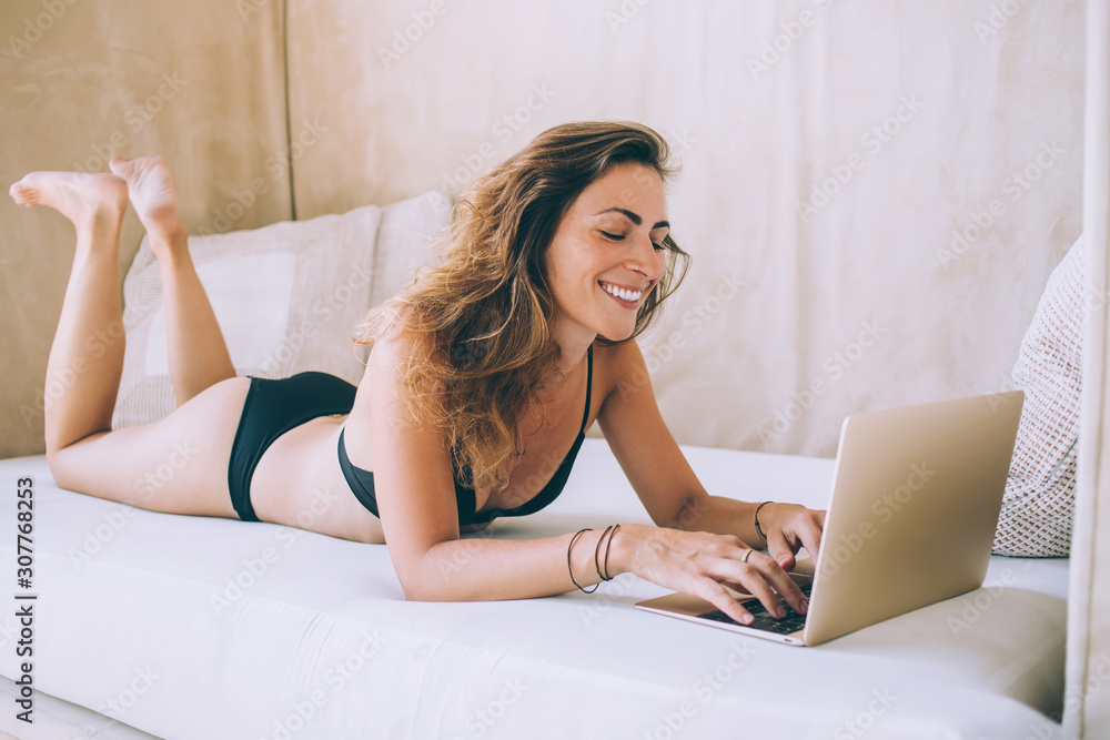 Smiling slim female in swimwear typing on laptop while lying on lounge spending vacation Smiling slim female in swimwear typing on laptop while lying on lounge spending vacation