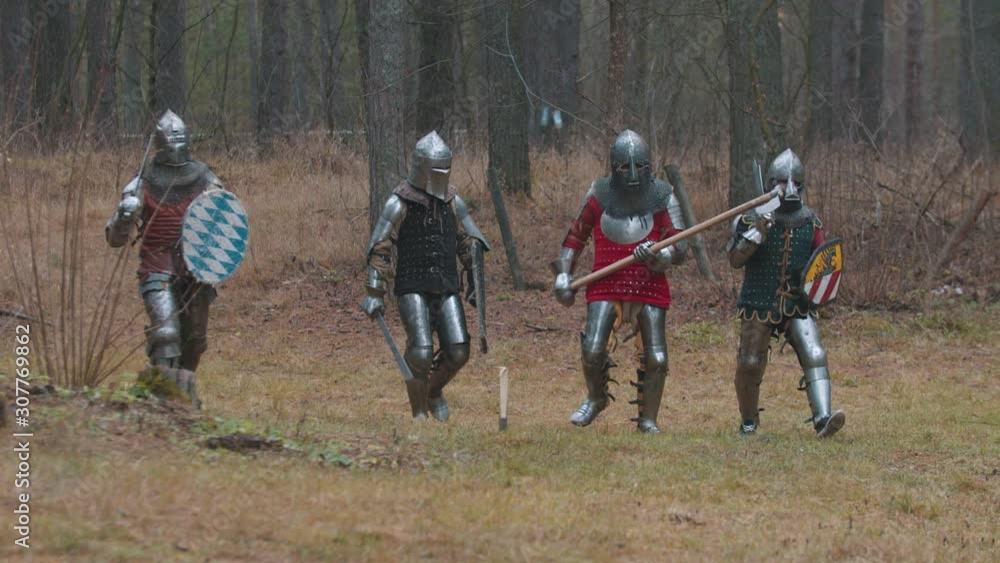 Four men knightes walking in the row in the forest in full armour Four men knightes walking in the row in the forest in full armour