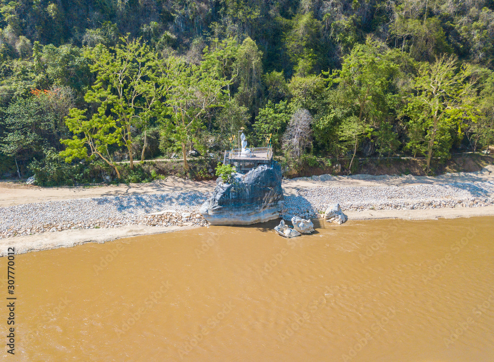 An iconic white Buddha statue on the rocky shore nearly Wat Tham Phra temple with Kok river view in Chiang Rai province of Thailand. An iconic white Buddha statue on the rocky shore nearly Wat Tham Phra temple with Kok river view in Chiang Rai province of Thailand.