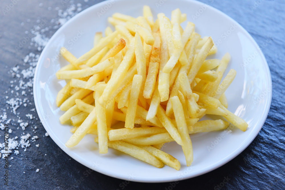 Fresh french fries and salt in white plate with black background - Tasty potato fries for food or snack delicious Italian meny homemade ingredients