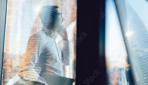 Businessman standing next to window and talking on phone