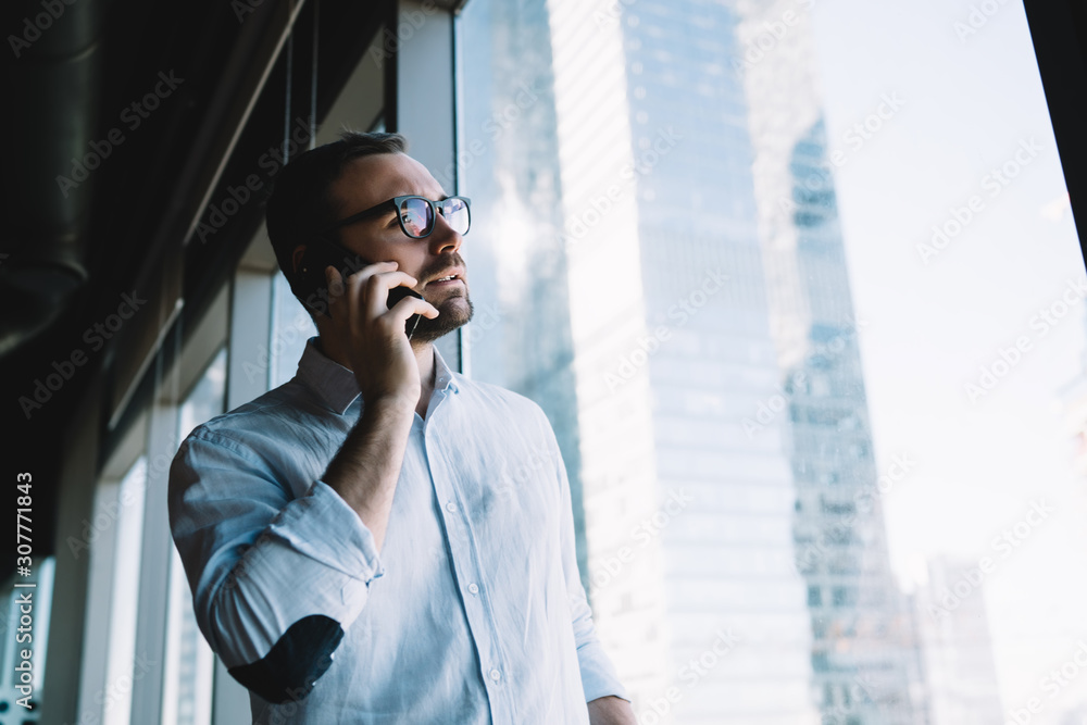Caucasian employer in classic spectacles for provide eyes protection using cellphone gadget for making service consultation during work day, young businessman calling to partner via cellular app Caucasian employer in classic spectacles for provide eyes protection using cellphone gadget for making service consultation during work day, young businessman calling to partner via cellular app