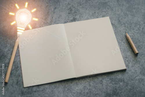 Fotografiet Pencils and plain notebook with light bulb futuristic icon on black background with copy space